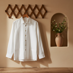 A white long-sleeve button-up shirt hangs on a wooden hanger from a brown collapsible wall coat rack, set against a warm beige wall with a built-in niche holding a vase of flowers and a wooden table below.