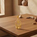 A single ornate gold-toned earring displayed on a wooden table in a warm, rustic interior setting with neutral decor in the background.