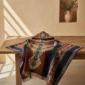 A hooded woven blanket or poncho with a large eagle motif and geometric border patterns, draped over a wooden table in a warm, sunlit room.