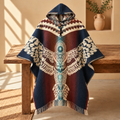 A hooded woven poncho with a large central bird motif and geometric border details, draped over a rustic wooden bench in a warm indoor setting.