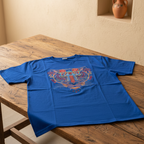 A royal blue short-sleeve t-shirt with a colorful embroidered tiger graphic on the front, laid flat on a rustic wooden table.