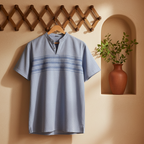 A light blue short-sleeve tunic shirt with horizontal textured stripe details across the chest, hanging on a wooden hanger against a warm beige stucco wall with a decorative wooden lattice and a potted plant in a recessed shelf.